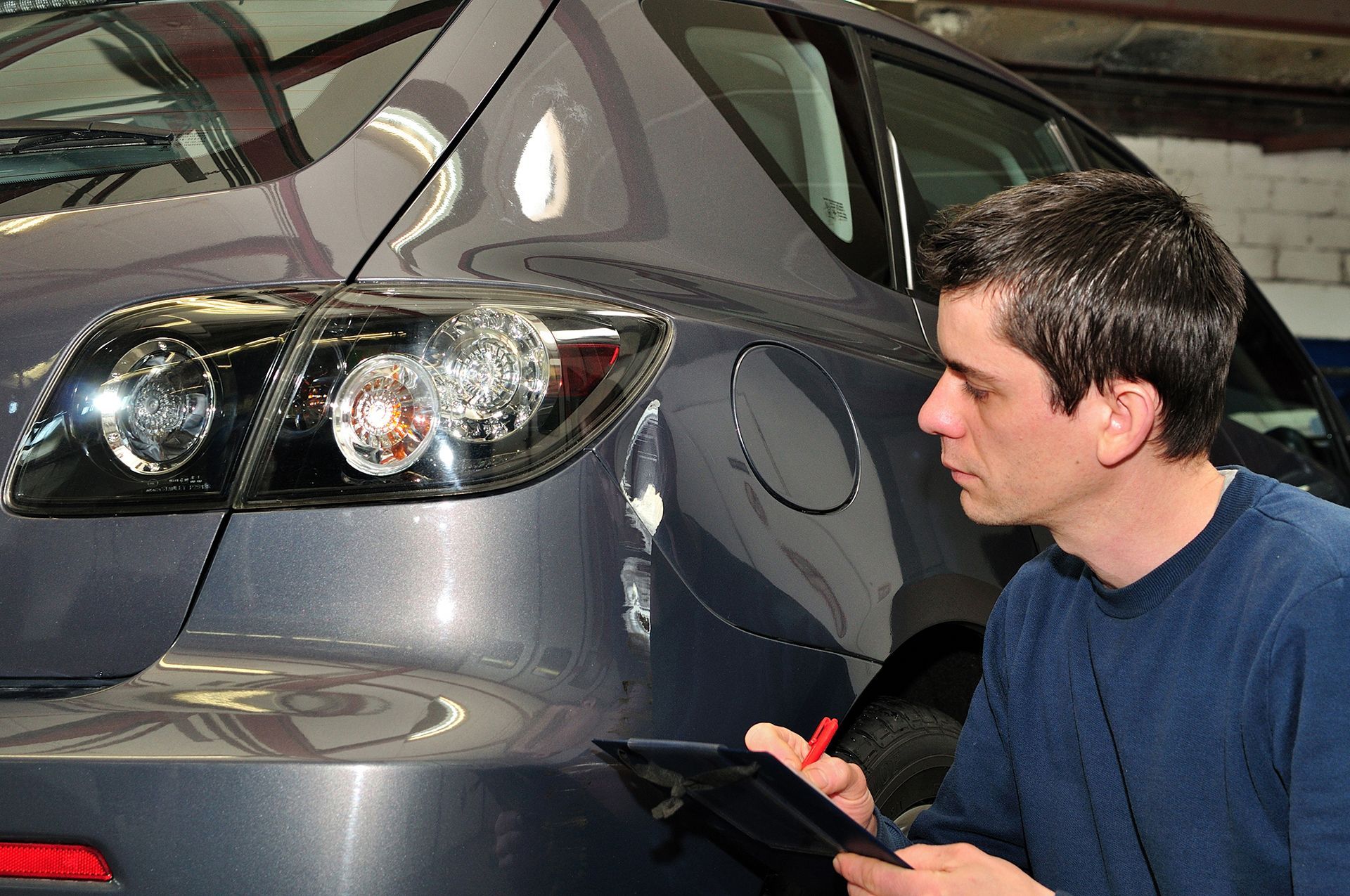 A man is writing on a clipboard in front of a car