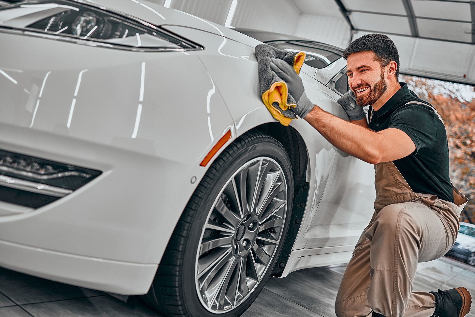 A man is cleaning a white sports car with a cloth.