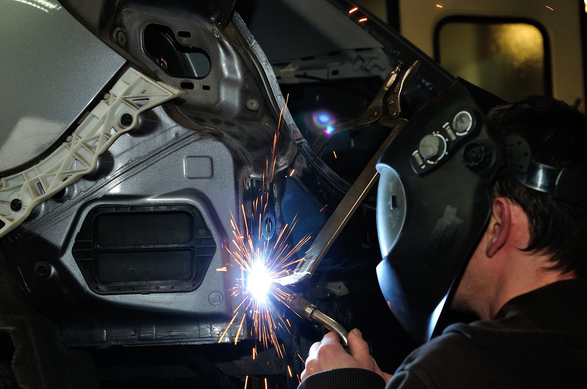 A man wearing a welding mask is welding a car