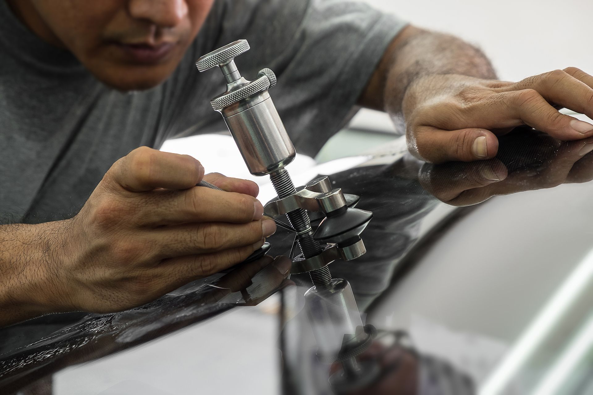 A man is repairing a windshield on a car with a tool.