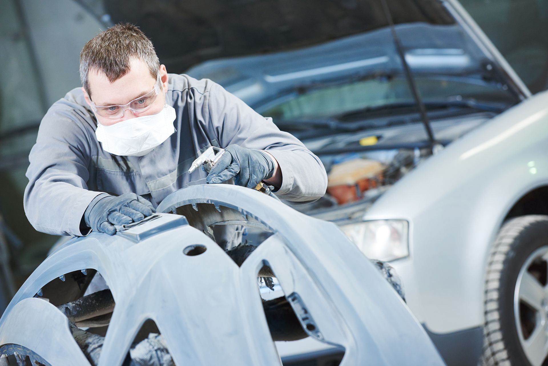 A man wearing a mask is working on a car.
