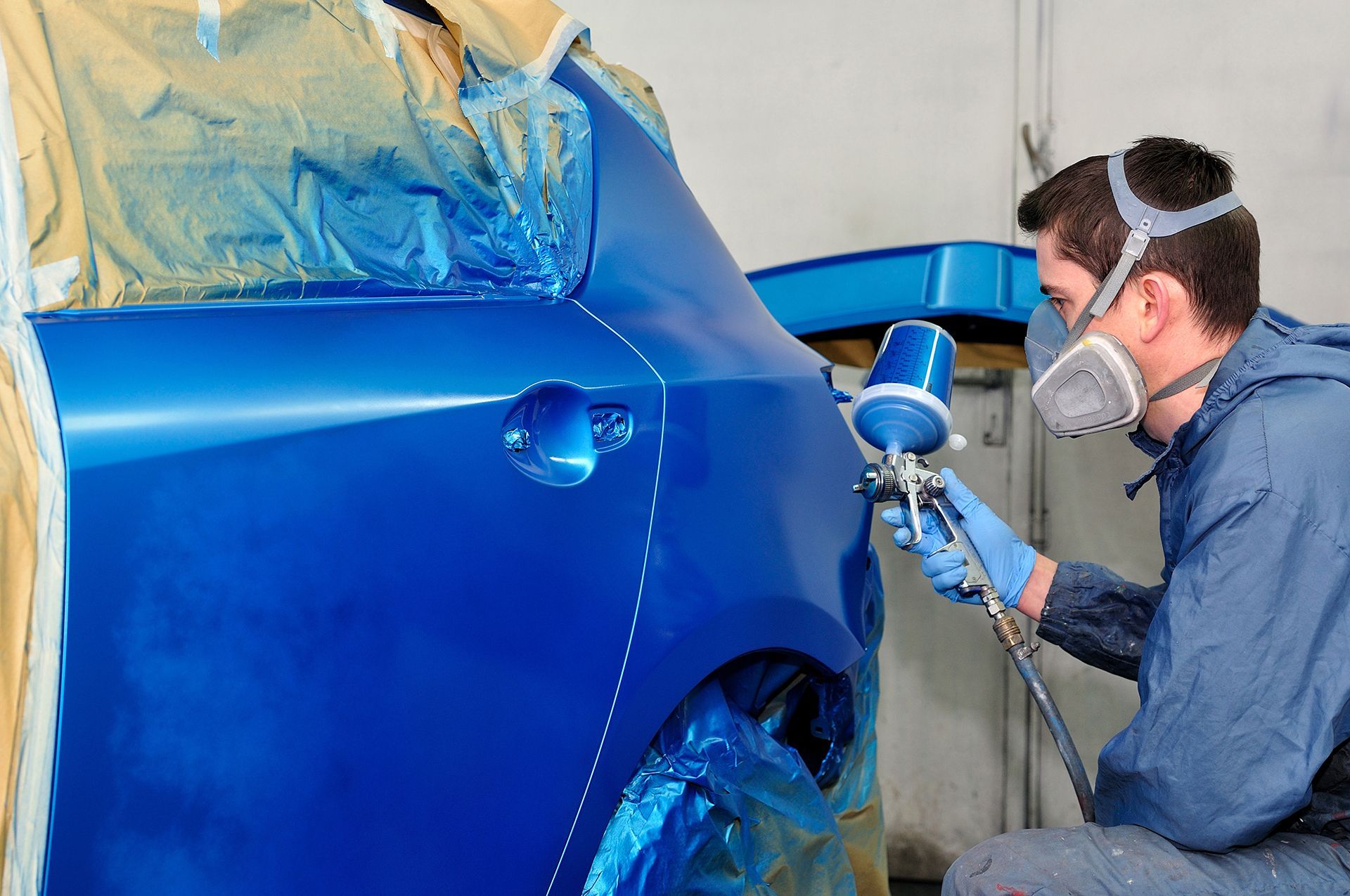 A man wearing a mask is spray painting a blue car.