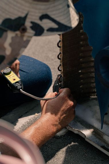 Hands working on a metal part with a measuring tape, outdoors on a textured surface.