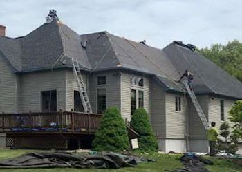 A group of people are working on the roof of a large house.