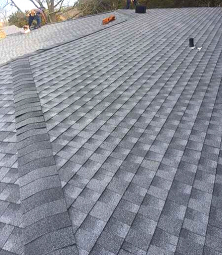 Gray asphalt shingles on a roof. A person stands on the roof edge.