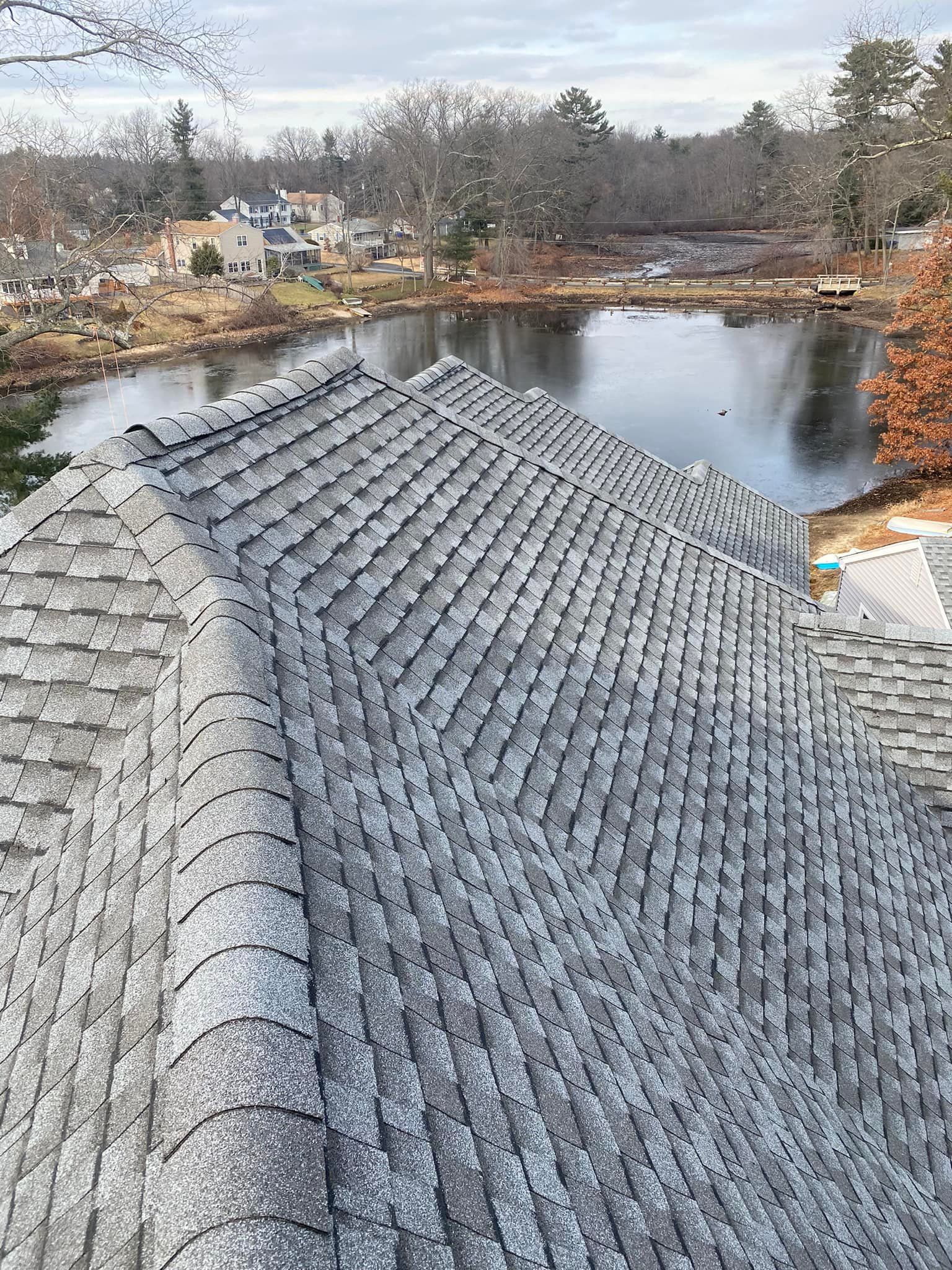 View of a gray shingle roof overlooking a lake on a cloudy day. Moss covers some of the shingles.