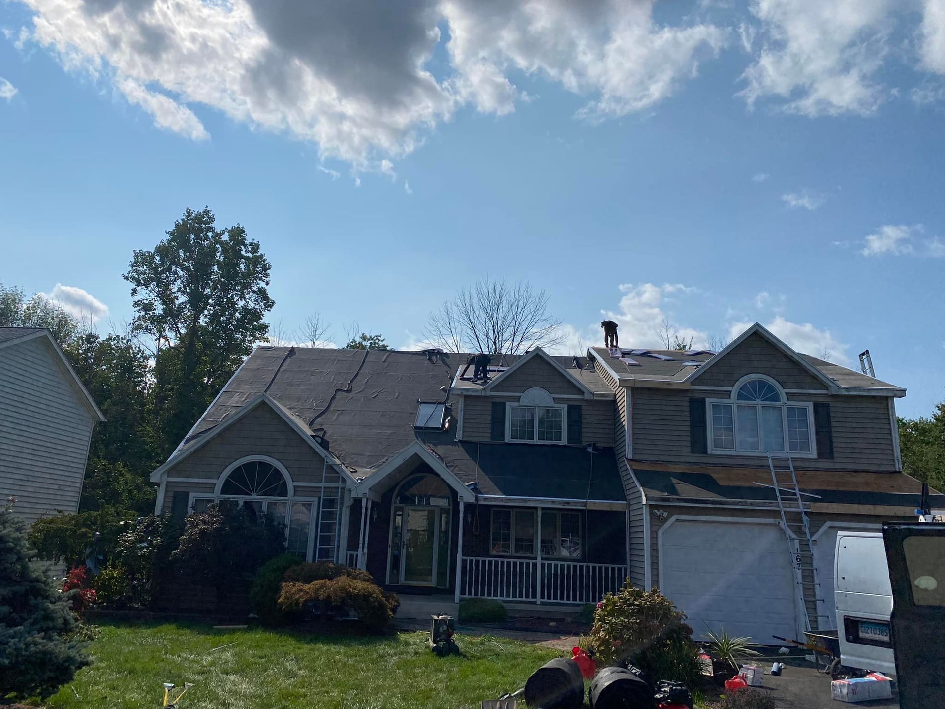 House with partially removed roof, likely undergoing repairs on a sunny day. Debris and a ladder are visible.