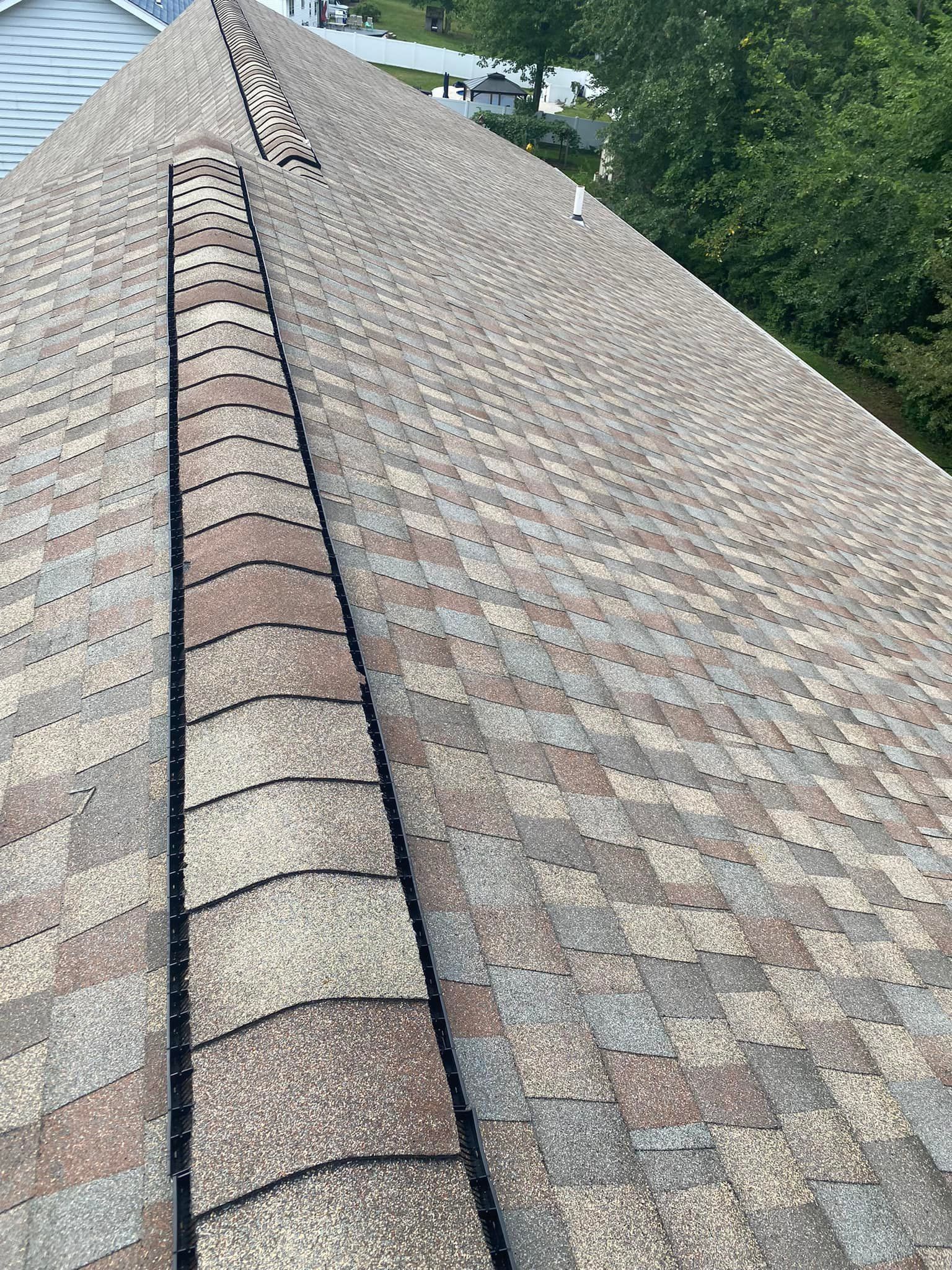 Close-up of a weathered shingle roof with a dark ridge line. The shingles are a mix of brown and grey tones.