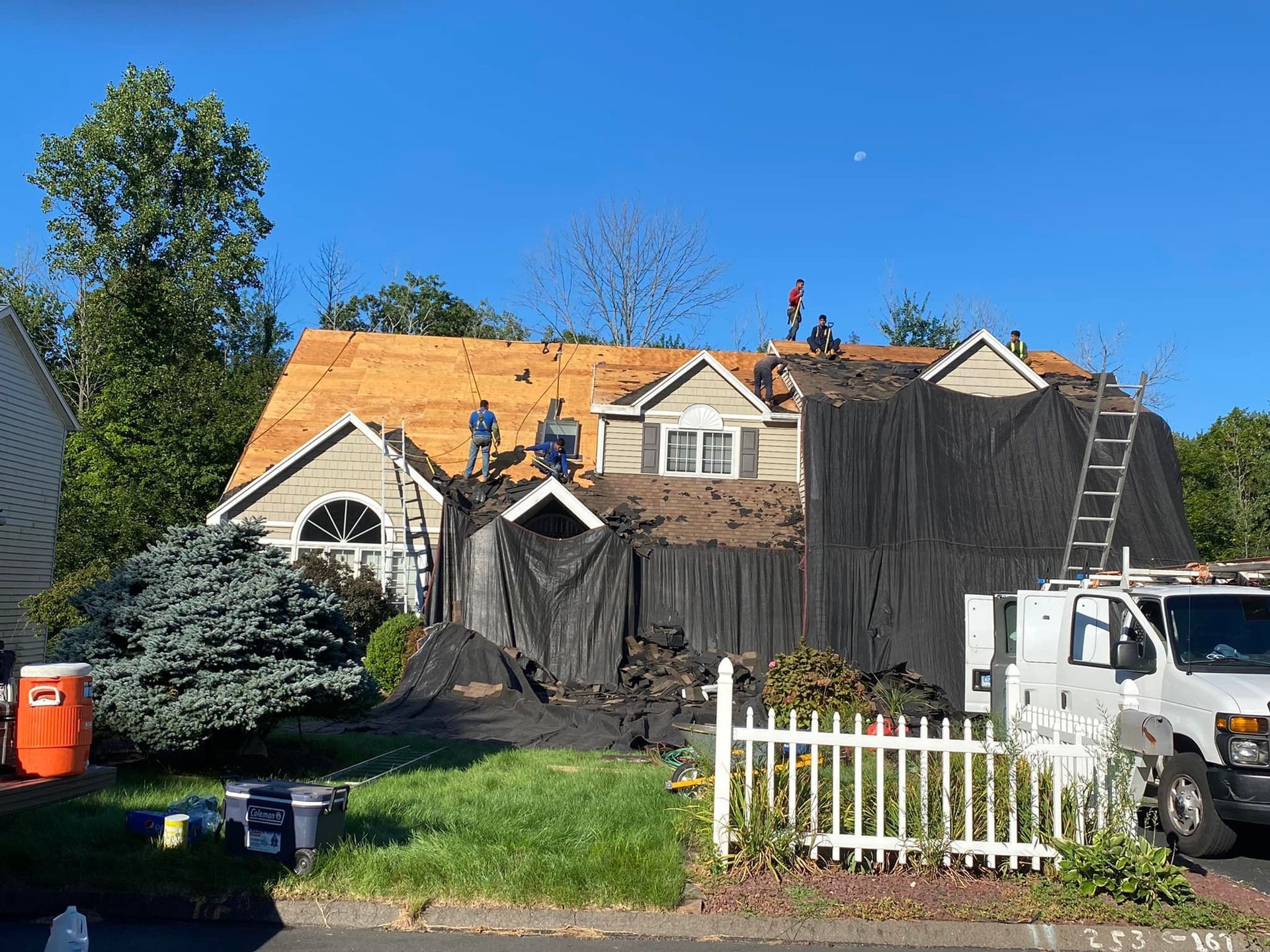 Roofers working on a house, removing old shingles and covering part of the roof with a tarp.