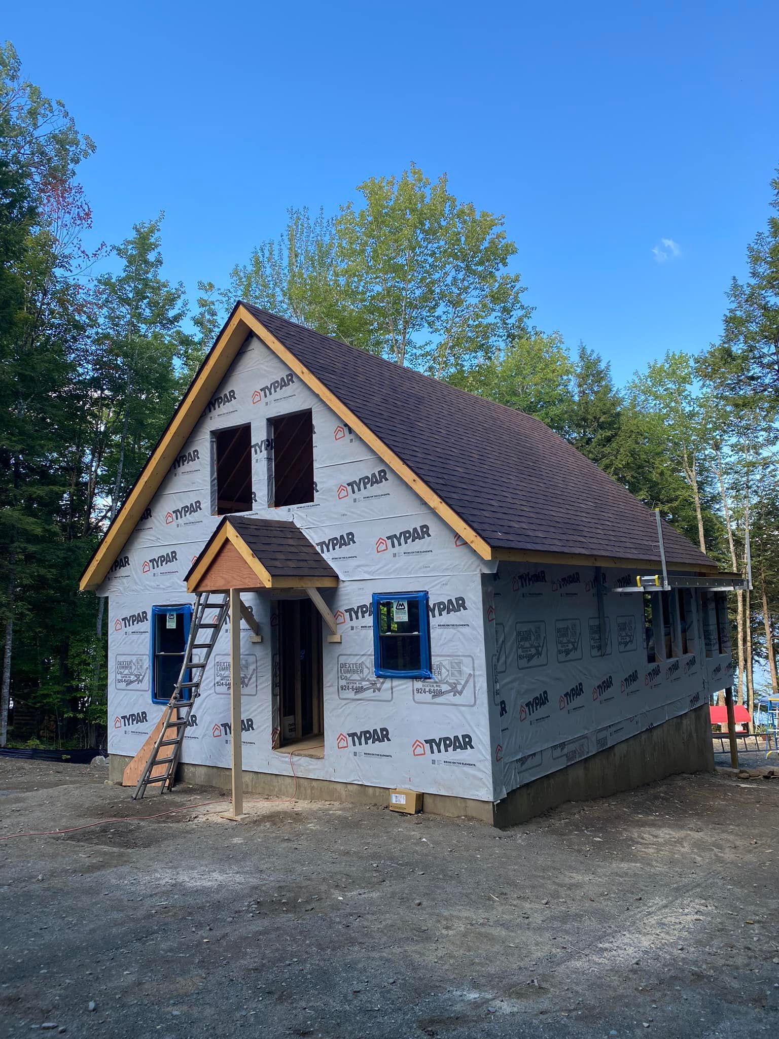 A house under construction, with a brown roof, gray siding, and blue window frames.