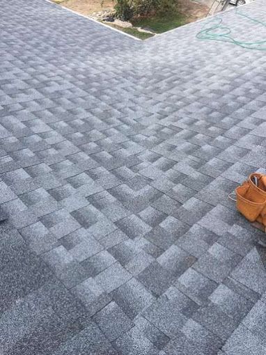 Close-up view of an asphalt shingle roof with a light and dark gray pattern, angled towards a roofline.