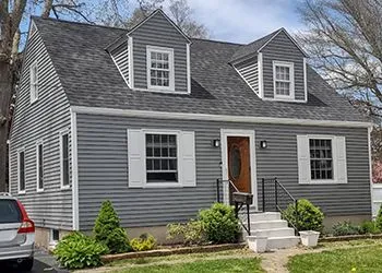 A gray two-story house with white trim, shutters, and three dormers. A car sits in the driveway.