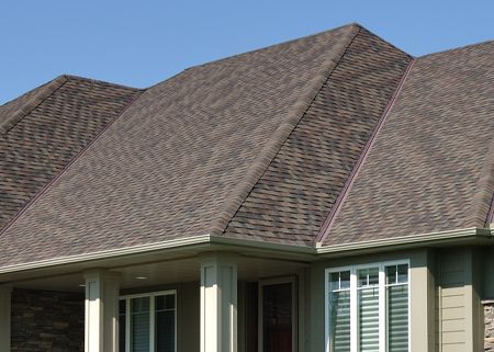Brown shingled roof on a house with white columns and windows against a blue sky.