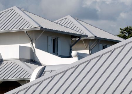 White metal roofs of a building on a cloudy day.  The roof sections are sloped, and a satellite dish is visible.