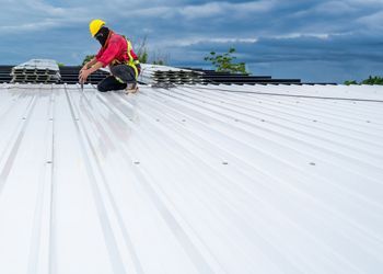 A man is kneeling on top of a white metal roof.