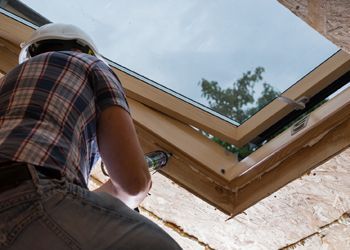 A man wearing a hard hat is working on a skylight.