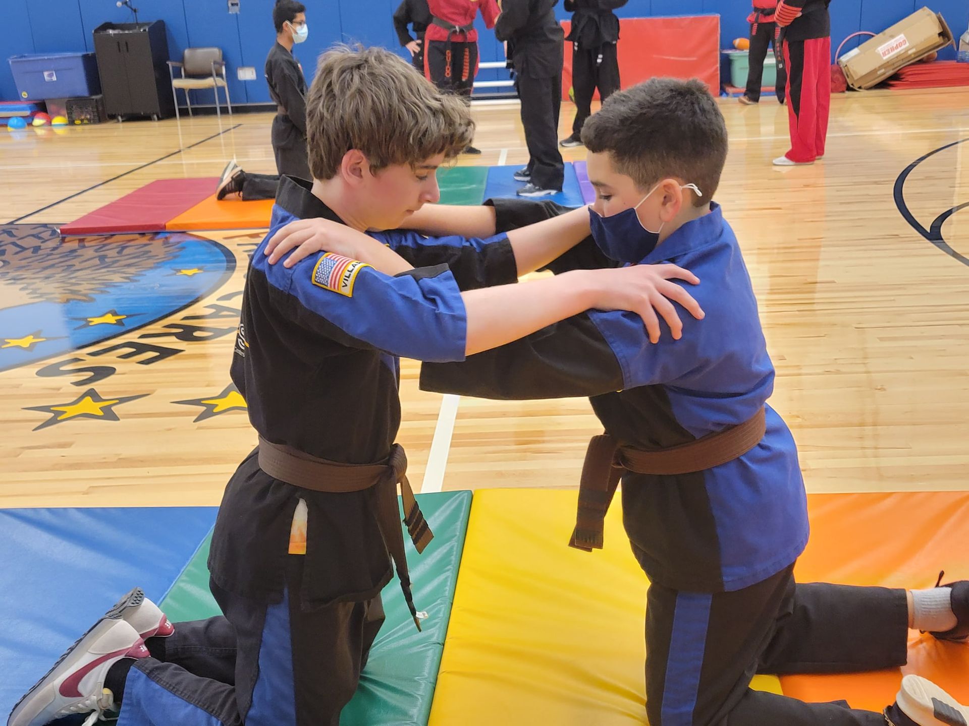 a group of kids in martial arts uniforms are standing on a wooden floor .