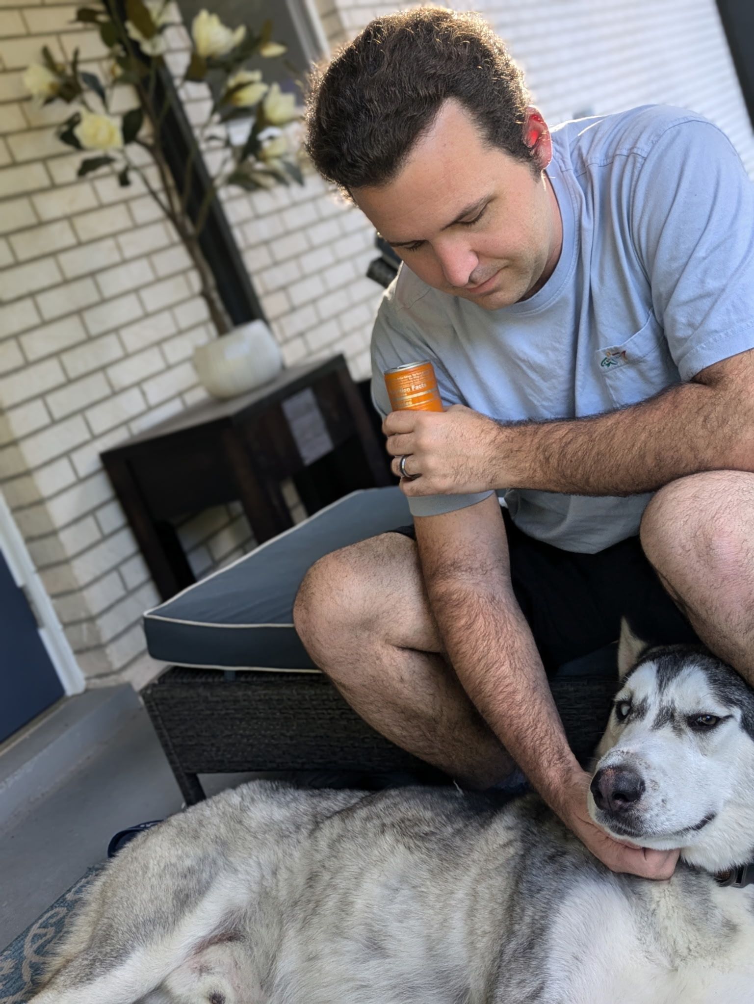 Man kneeling, petting a gray and white Husky on a porch.