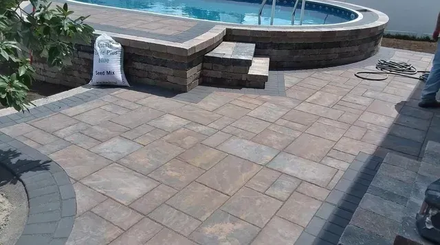 A man is working on a patio next to a swimming pool.