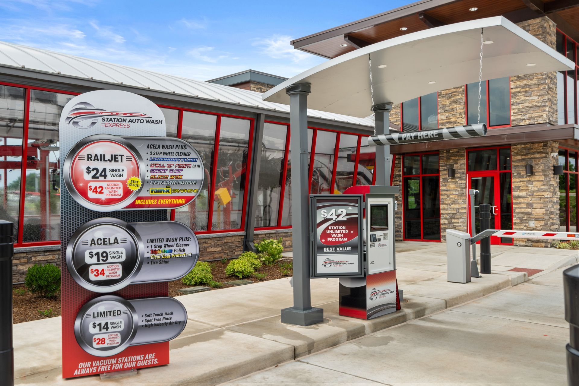 A car wash with price signs; entrance with a kiosk and barrier. Building exterior in the background.
