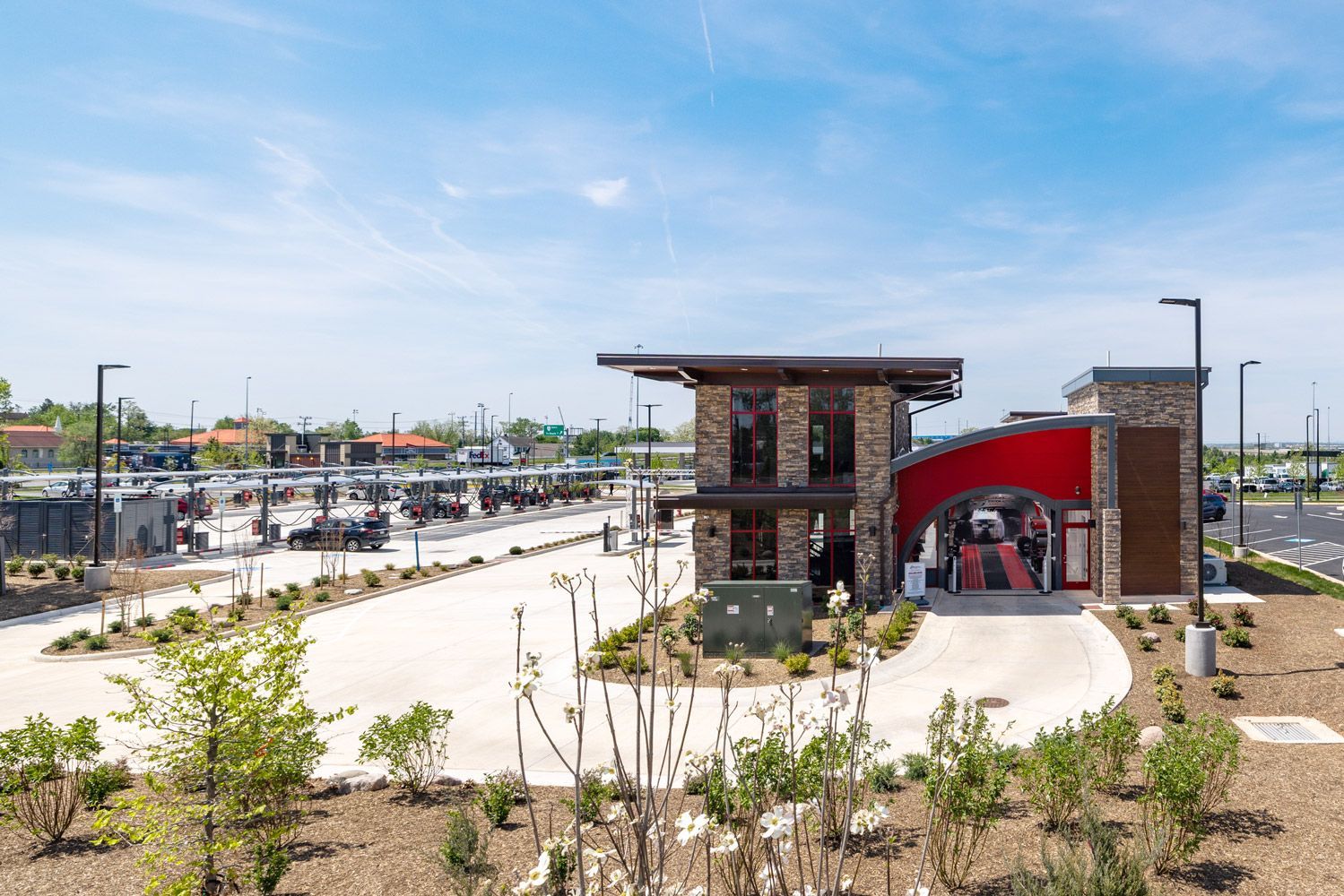 A large building with a red roof is surrounded by trees and a parking lot.