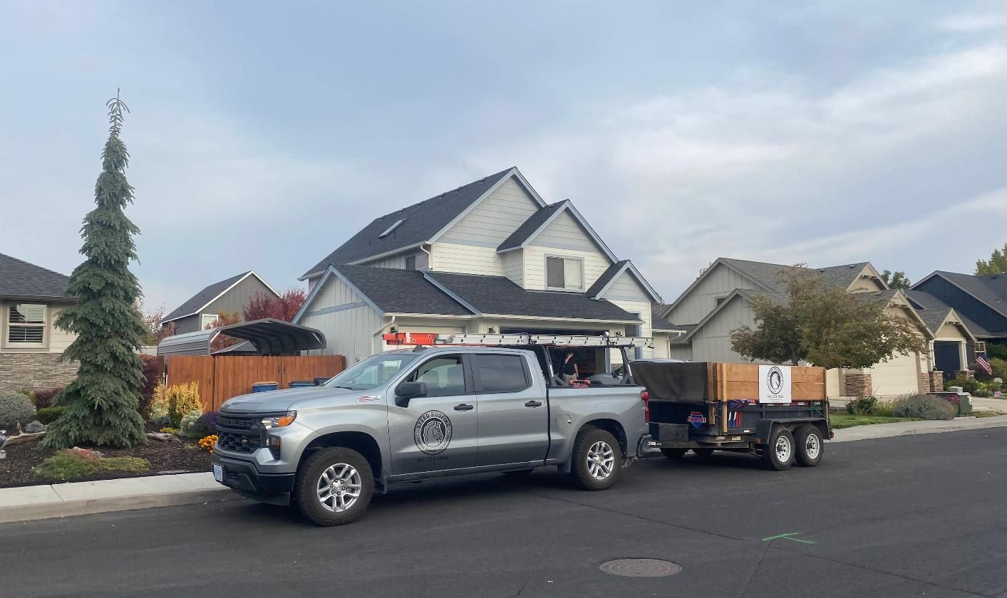A dark gray asphalt shingle roof on a house with vents, surrounded by trees on a cloudy day.