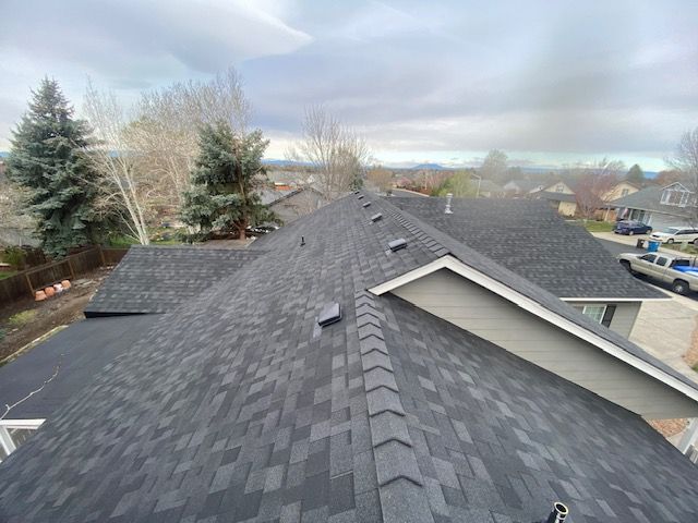Dark gray asphalt shingle roof on a house with a cloudy sky backdrop.