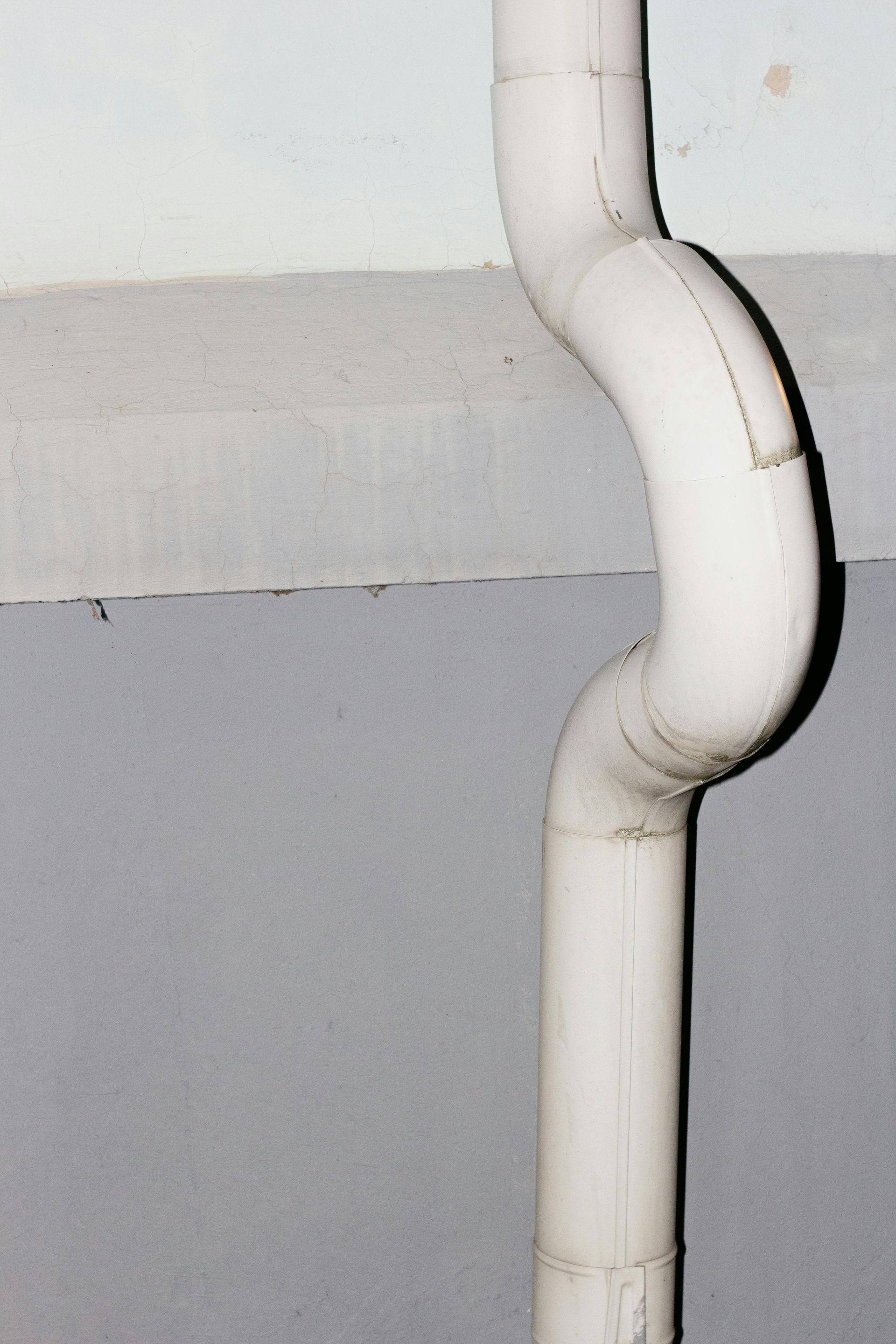 White downspout curves against a gray wall.