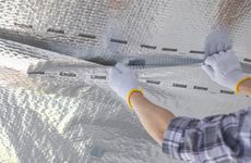 Person wearing gloves installing reflective insulation.