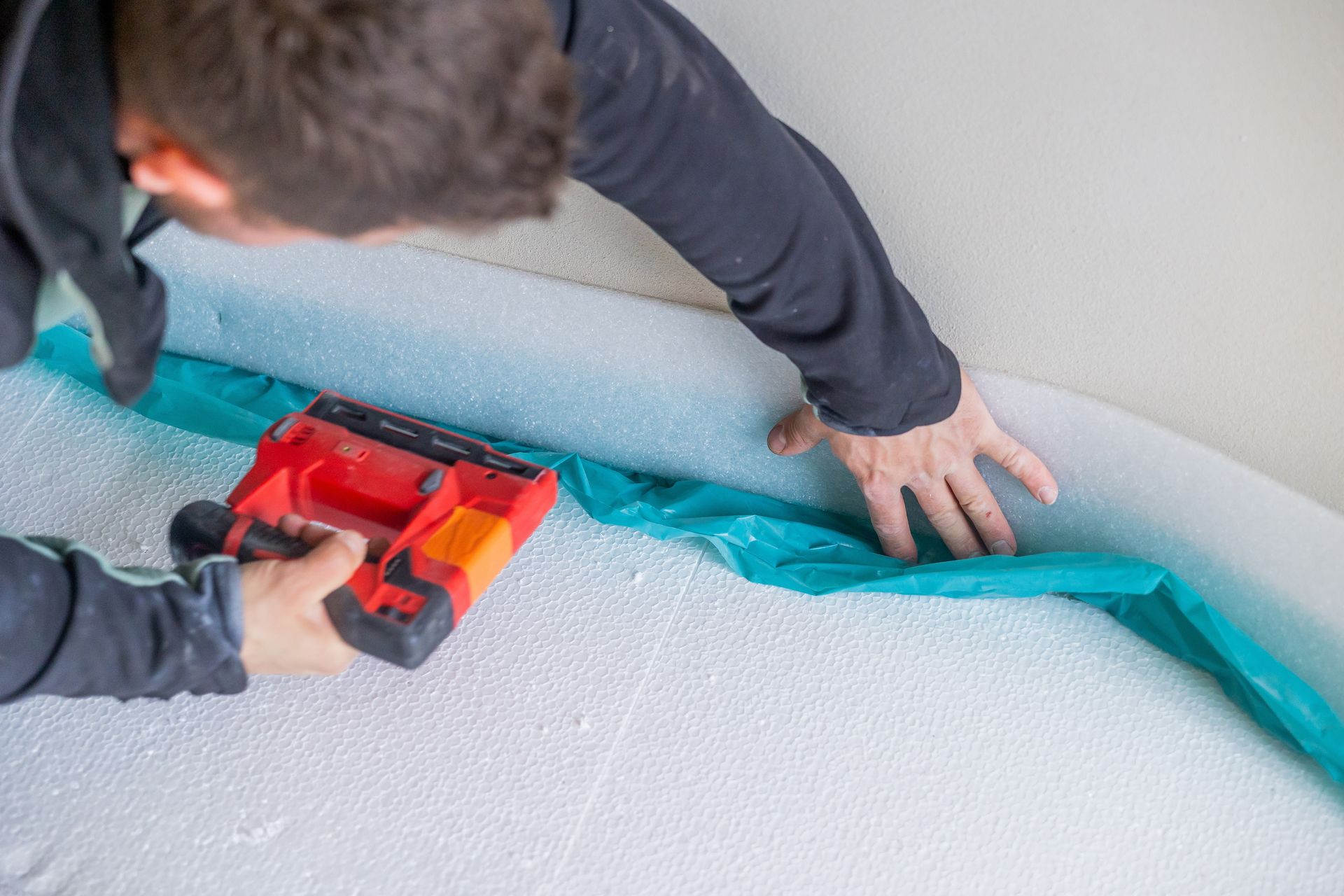 Person installing blue material with a red stapler on a white, curved surface.