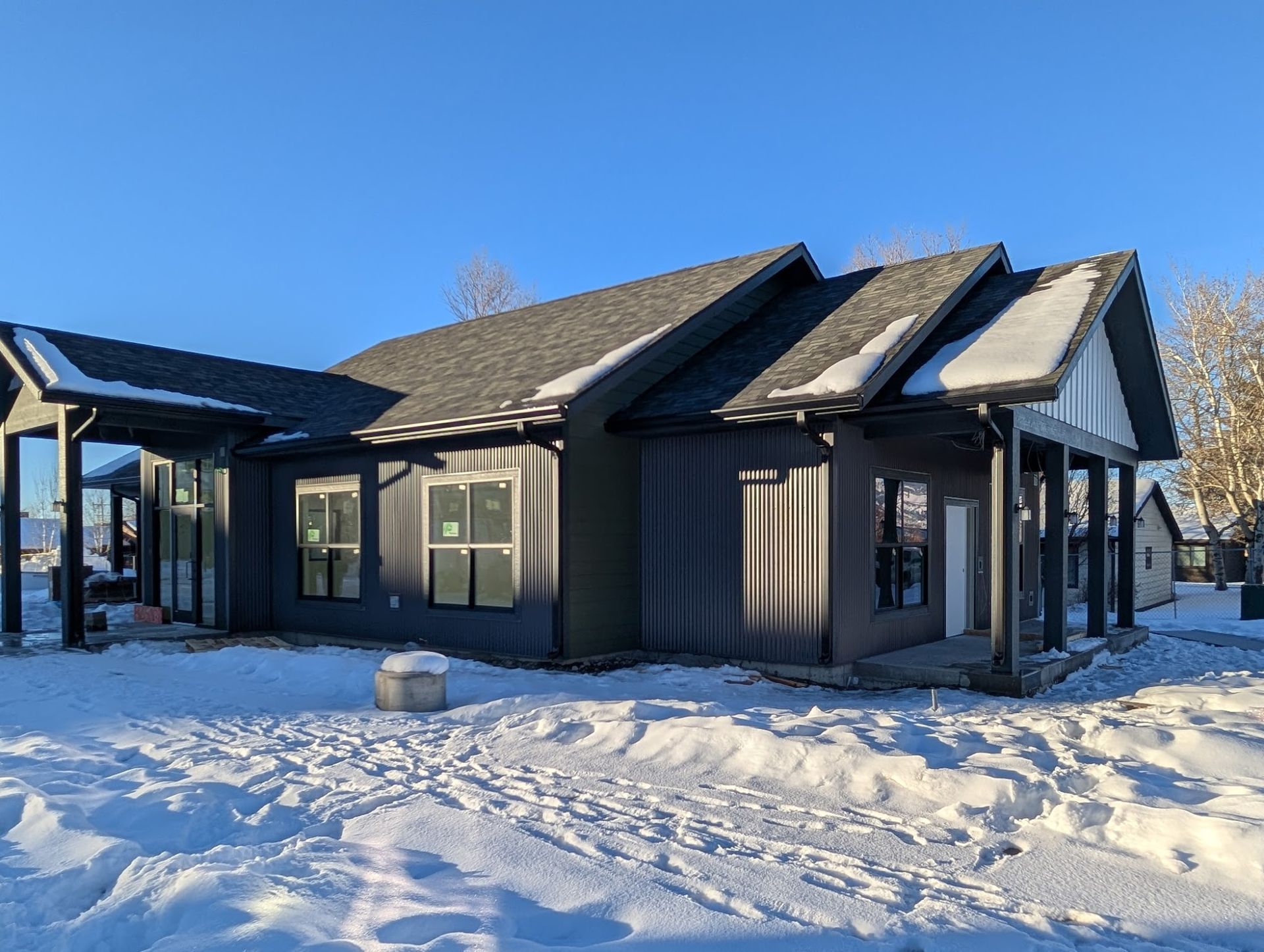 Dark gray house with snow-covered ground and blue sky.