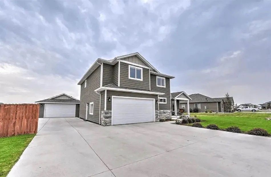 Two-story gray house with attached garage, long driveway, and detached garage; cloudy sky.