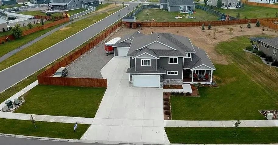 An aerial view of a gray two-story house with a white garage door and a long driveway.