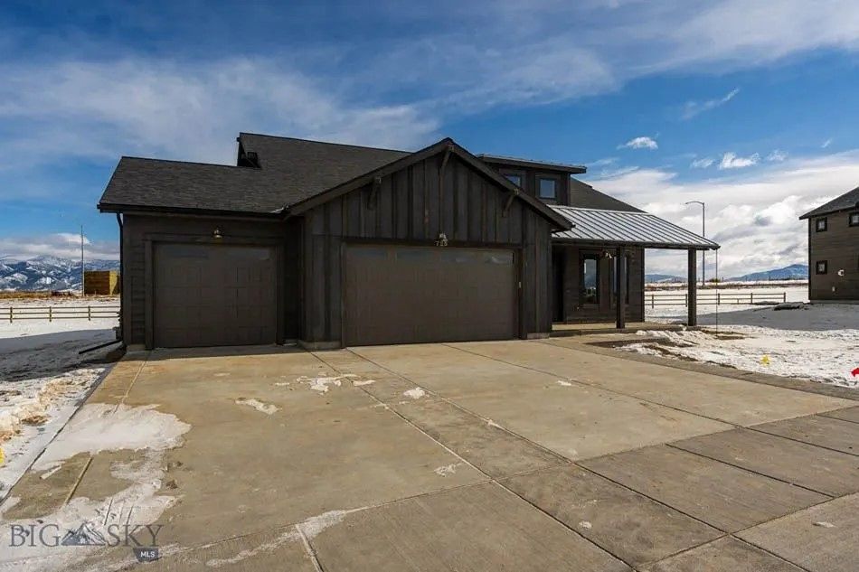 Dark gray house with a two-car garage, porch, and snow on the ground under a blue sky.