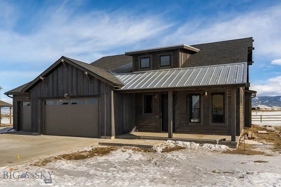 Dark gray modern house with garage and metal roof, against a blue sky, snow in the foreground.