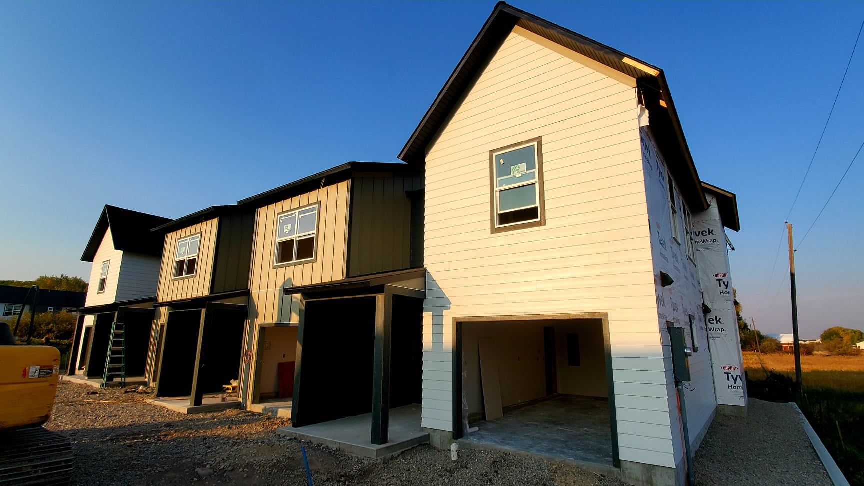 Row of new townhomes under construction, featuring different colored siding and an open garage.