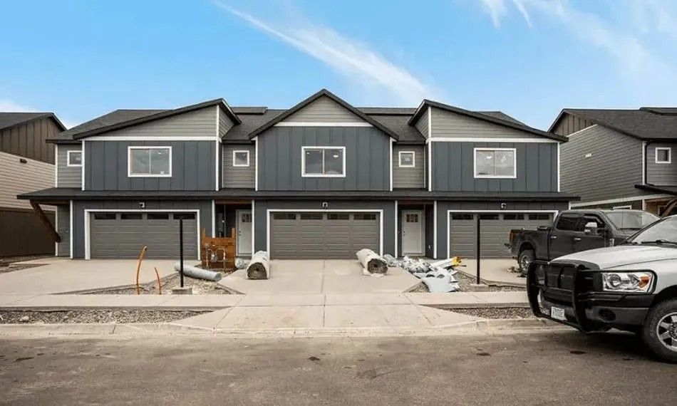 Three connected townhouses with gray siding, attached garages, and a construction site.