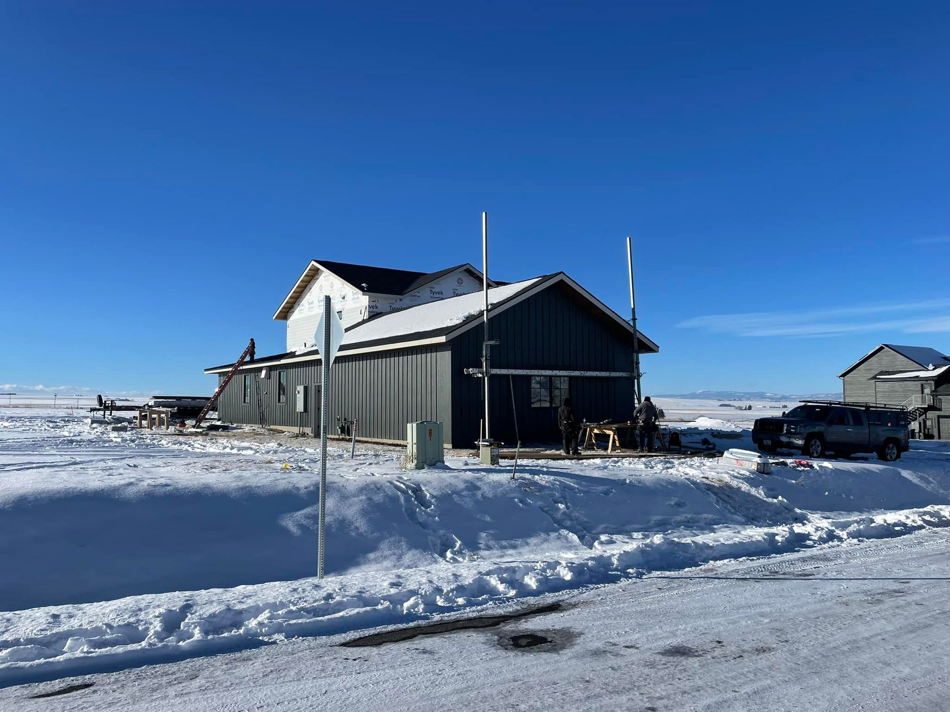 Snowy landscape with a blue house and dark outbuildings. A car is parked nearby under a clear sky.