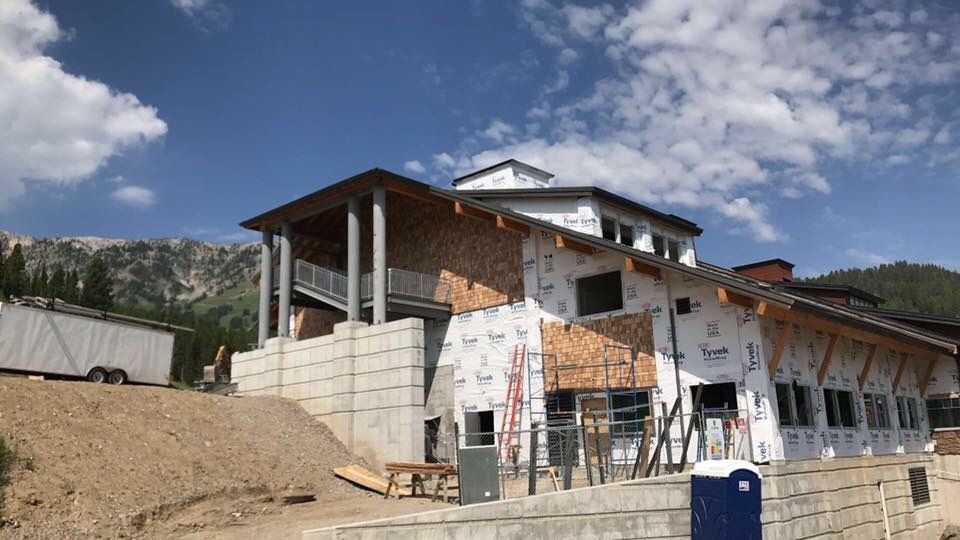 Building under construction with wood and white wrap, mountains in background.