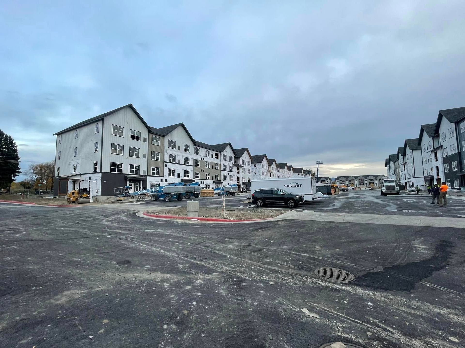 Construction site with multiple new apartment buildings under cloudy skies; trucks and equipment visible.
