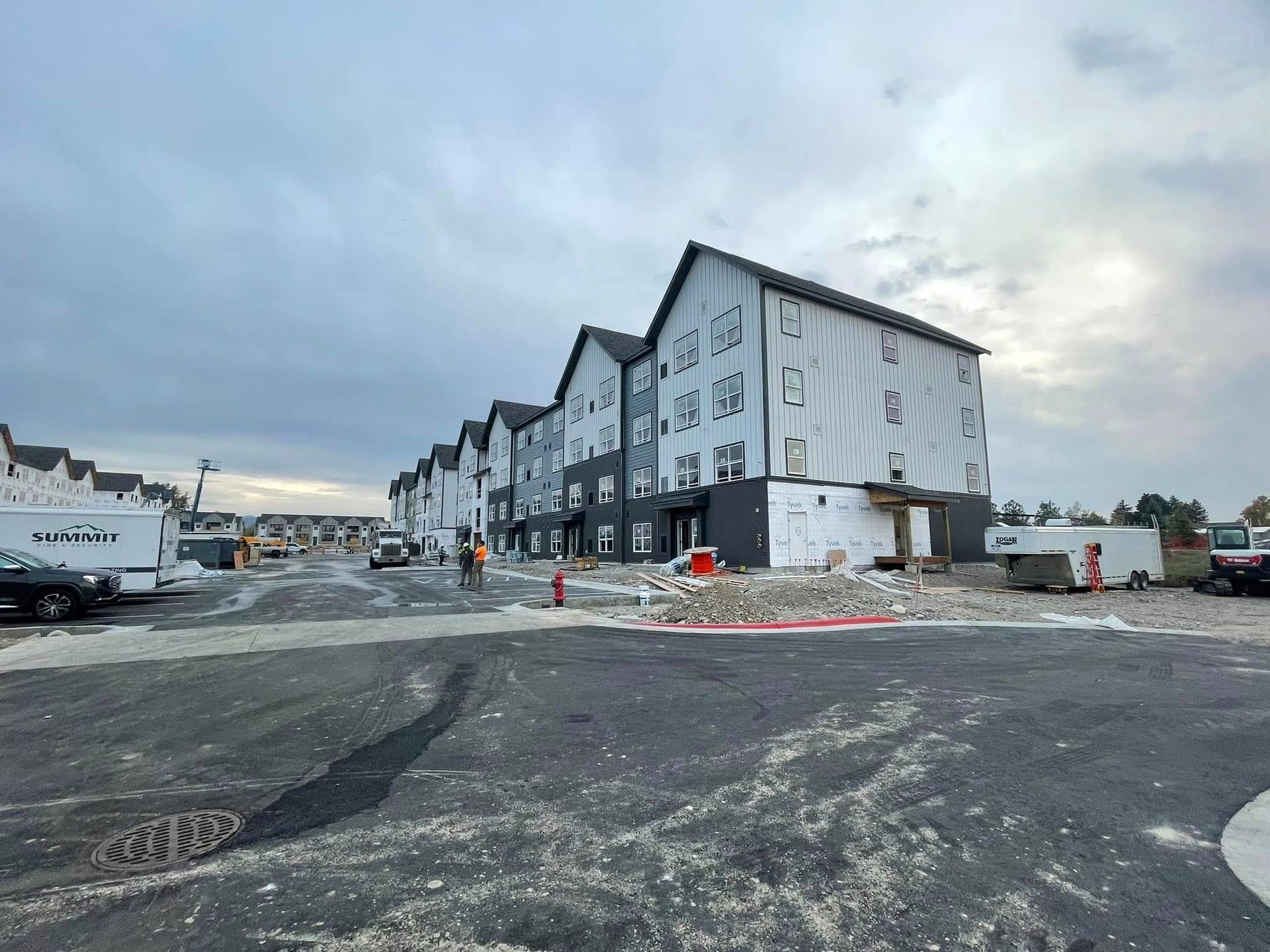 Construction site: Multi-story townhomes with black and white siding under cloudy sky.