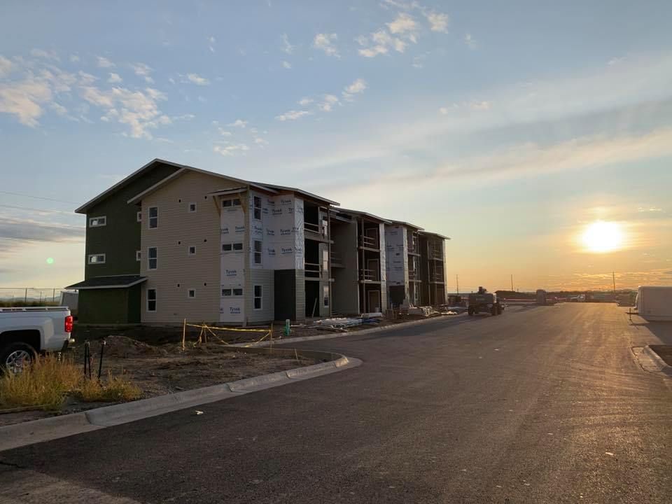 Apartment building under construction at sunset with blue sky, unfinished siding, and a paved road.