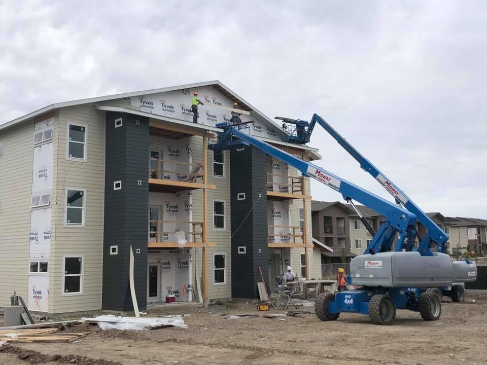 Construction workers on roof of building, one in boom lift, beige siding, gray sky.