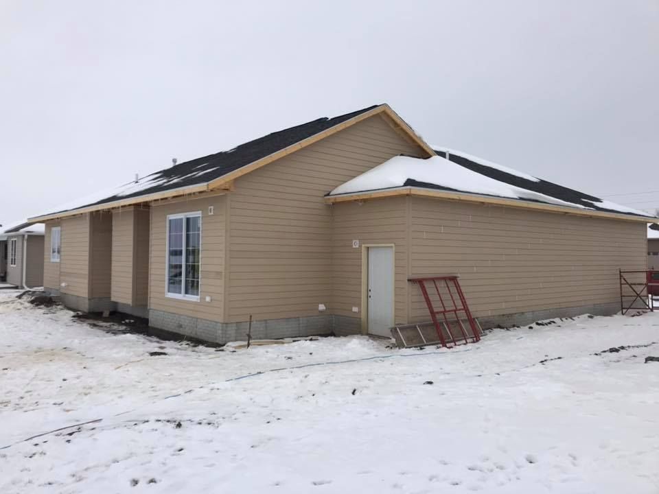 Tan-sided house under construction in a snowy setting; visible window, door, and unfinished roof.