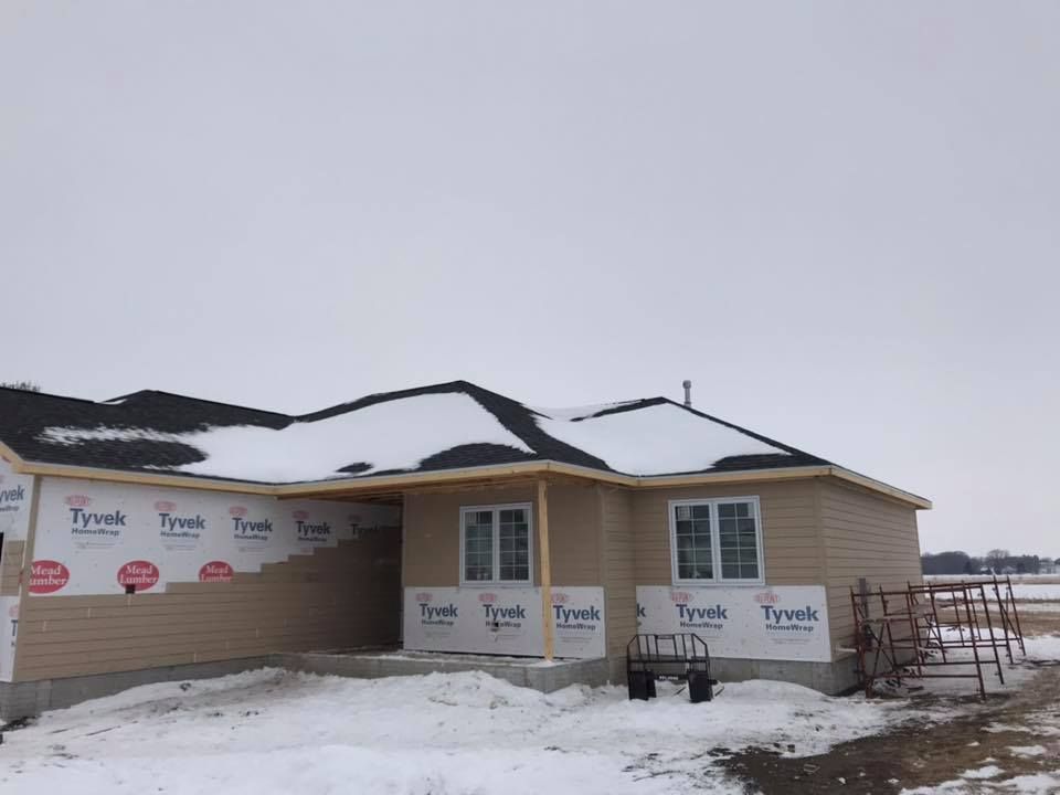 House under construction with tan siding and Tyvek wrap, snowy ground.
