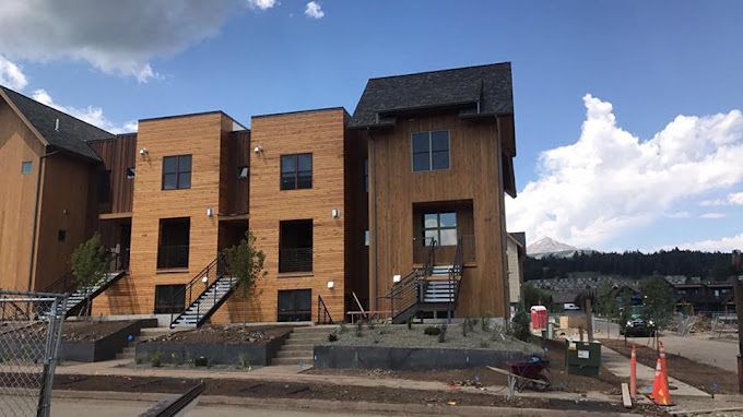 Modern townhouses with wood siding under a blue sky, construction in foreground.