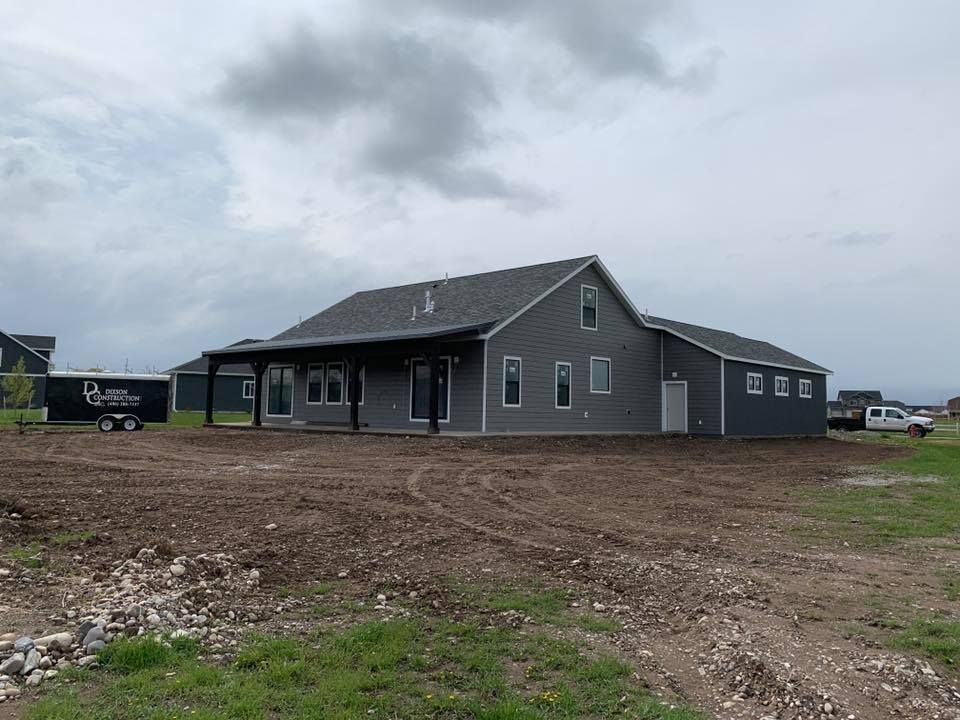 Gray-sided house under construction with a dark roof and a covered porch on a cloudy day.