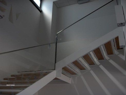 Scala con ringhiera in vetro, travi di sostegno bianche e gradini in legno naturale.
