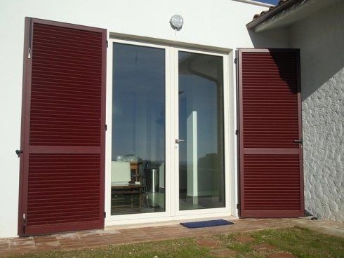 Persiane rosse che fiancheggiano una porta a vetri doppia
