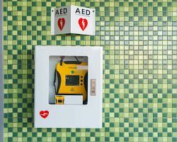 AED in a white cabinet on a green tiled wall, with a heart symbol and AED signage.